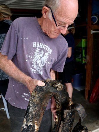 A man holds a partially-decomposed tyre with sea life growing on it. |340x453