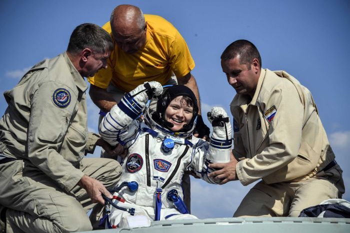 Anne McClain is all smiles as ground staff help her out of the capsule after landing