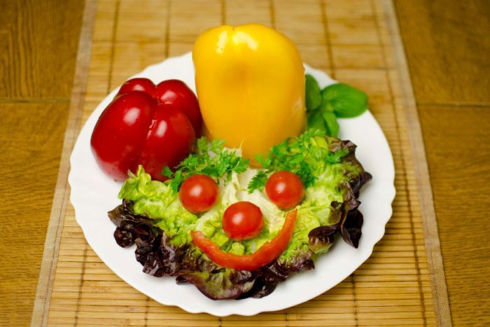A plate with lettuce leaves with a smiley face made up of tomato and capscium.|700x467