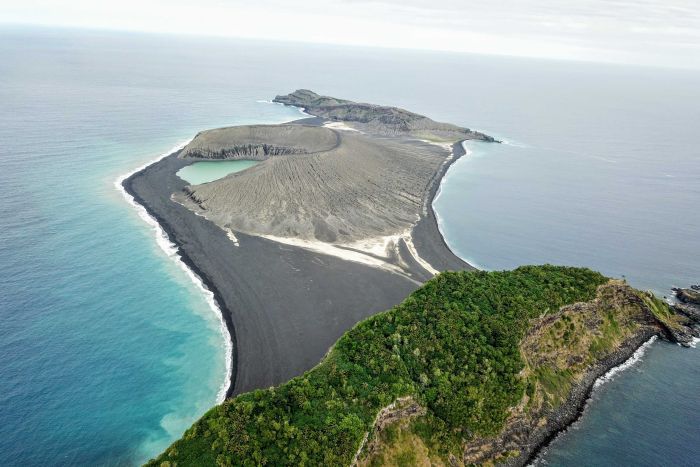 A grey volcanic island pictured from above and connected by an isthmus to an older island covered in vegetation|700x467