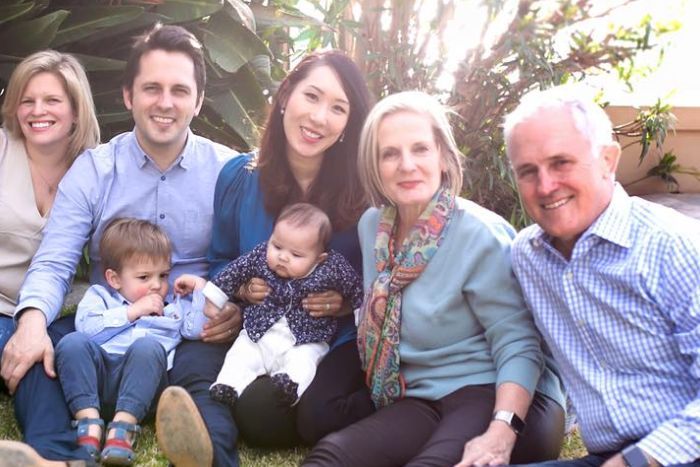 Malcolm Turnbull sits on the grass with wife, his adult children and their partners, and two babies, smiling at the camera|700x467