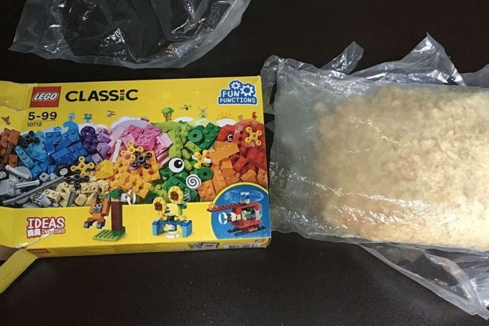 A Lego box next to a bag of a light-brown crystal substance, sealed in plastic packaging. |700x467