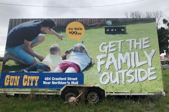 A large advertising billboard depicting a family with young children using air rifles outside|700x467