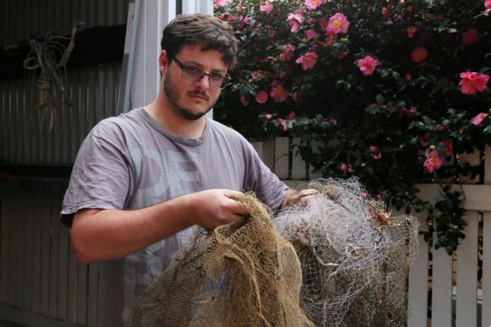A man holds old casting nets in front of a shed. |700x467