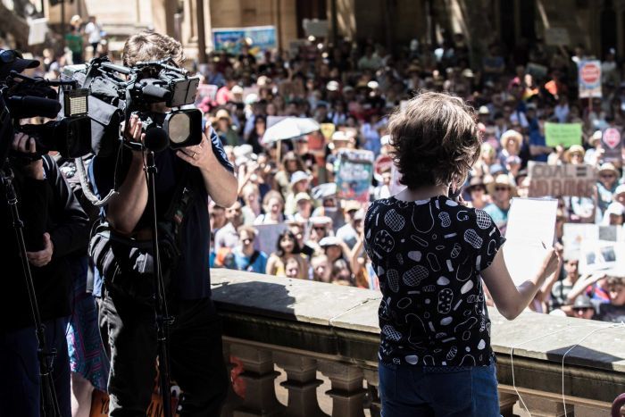 young girl speaking to audience with TV cameras filming her|700x467